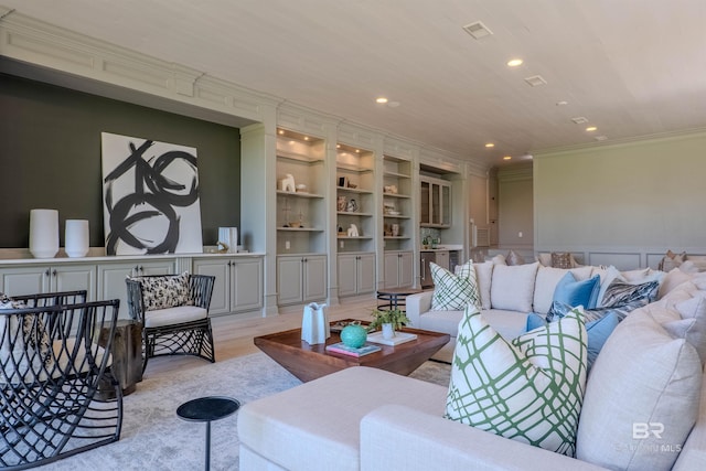 living room featuring built in features, ornamental molding, and light hardwood / wood-style flooring