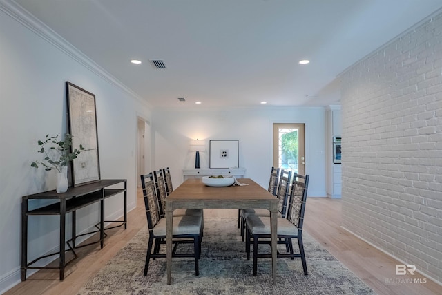 dining area with light hardwood / wood-style flooring, ornamental molding, and brick wall