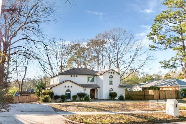 mediterranean / spanish-style house featuring a fenced front yard, a chimney, and stucco siding