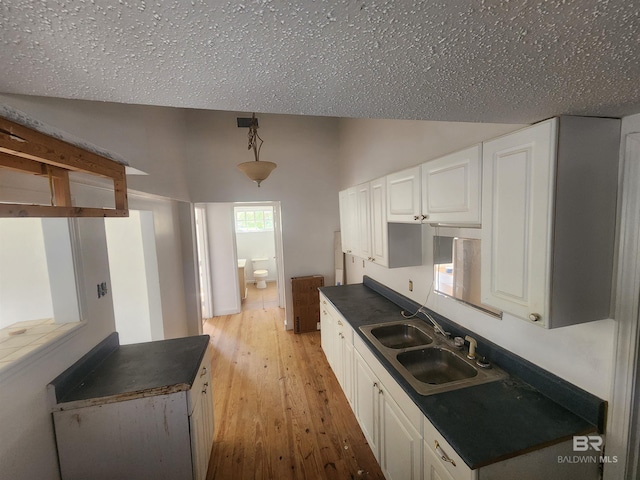 kitchen with sink, pendant lighting, a textured ceiling, white cabinets, and light wood-type flooring