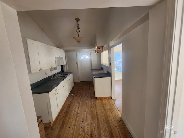 kitchen featuring sink, light hardwood / wood-style flooring, vaulted ceiling, decorative light fixtures, and white cabinets