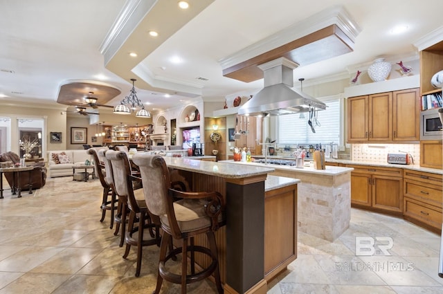 kitchen featuring crown molding, island range hood, a center island, appliances with stainless steel finishes, and a kitchen breakfast bar