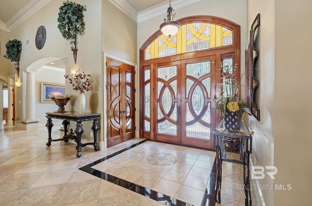 foyer entrance with decorative columns, crown molding, and a high ceiling