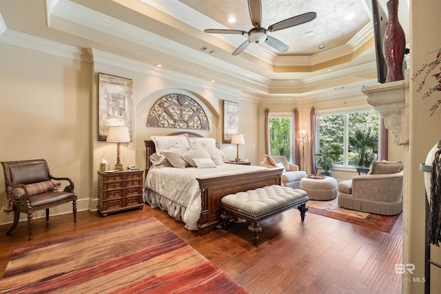 bedroom featuring hardwood / wood-style flooring, ornamental molding, ceiling fan, and a tray ceiling