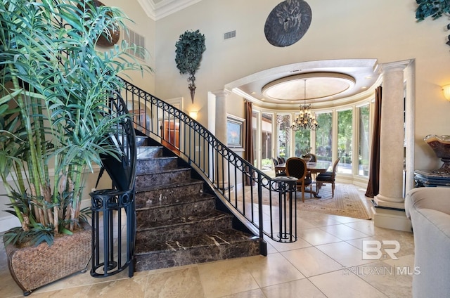 stairs featuring ornate columns, a chandelier, a high ceiling, crown molding, and tile patterned floors