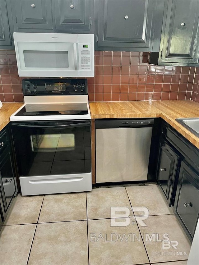 kitchen featuring decorative backsplash, light tile patterned flooring, wood counters, and white appliances