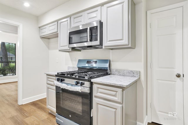 kitchen featuring stainless steel appliances, light wood-style flooring, baseboards, light stone counters, and white cabinetry