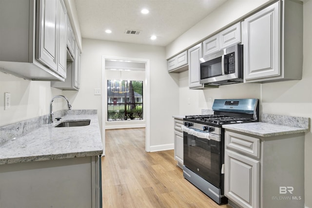 kitchen with appliances with stainless steel finishes, a sink, light wood finished floors, recessed lighting, and light stone countertops