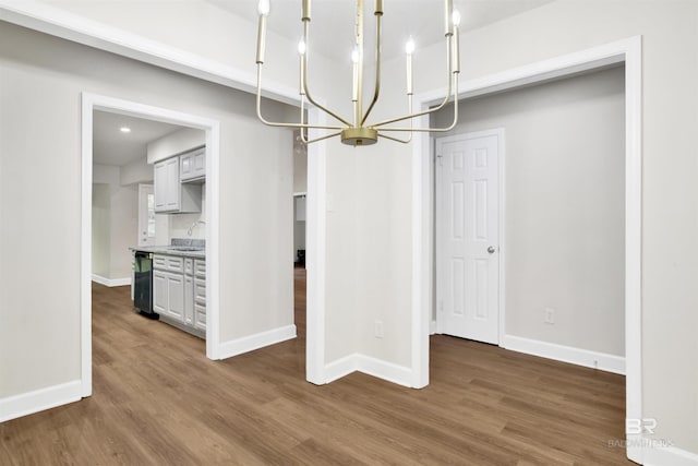 unfurnished dining area with a chandelier, wood finished floors, a sink, and baseboards