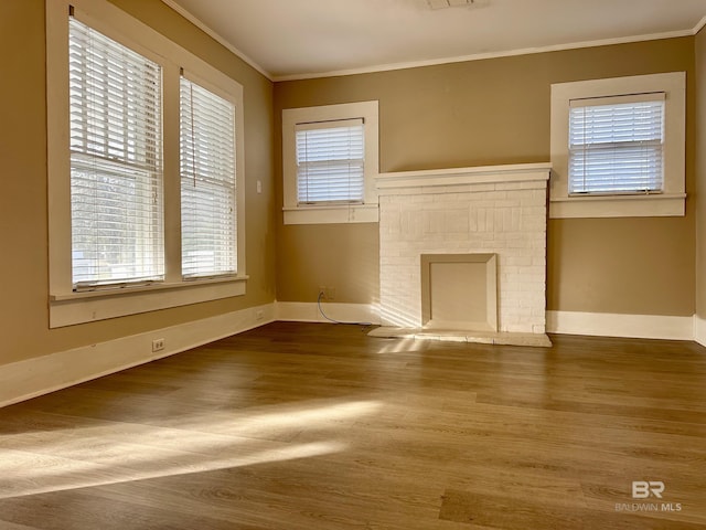 unfurnished living room with hardwood / wood-style floors, ornamental molding, a fireplace, and a wealth of natural light