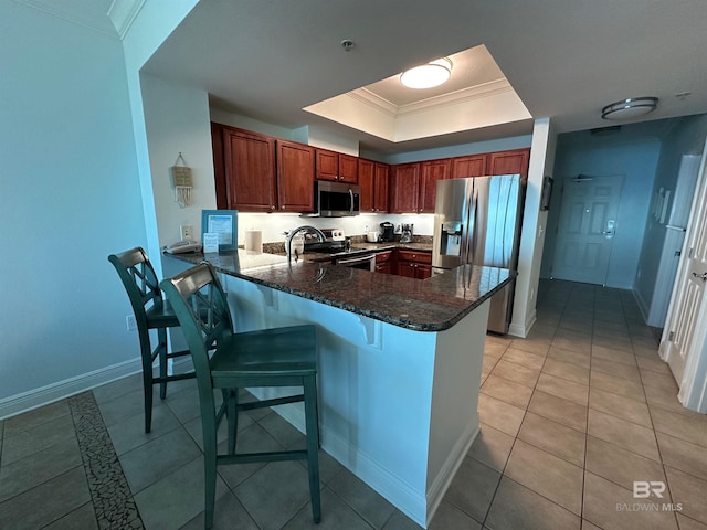 kitchen featuring ornamental molding, dark stone counters, appliances with stainless steel finishes, a peninsula, and light tile patterned flooring