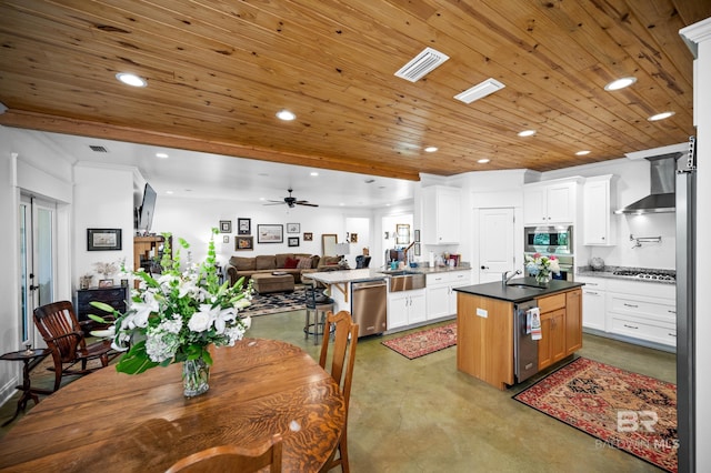 kitchen with kitchen peninsula, stainless steel appliances, wall chimney range hood, a center island, and white cabinetry