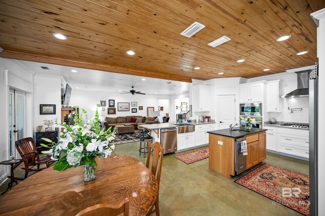 kitchen with a center island, white cabinetry, wall chimney range hood, stainless steel appliances, and kitchen peninsula