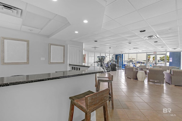 kitchen with light tile patterned floors, a drop ceiling, dark stone countertops, a breakfast bar area, and floor to ceiling windows