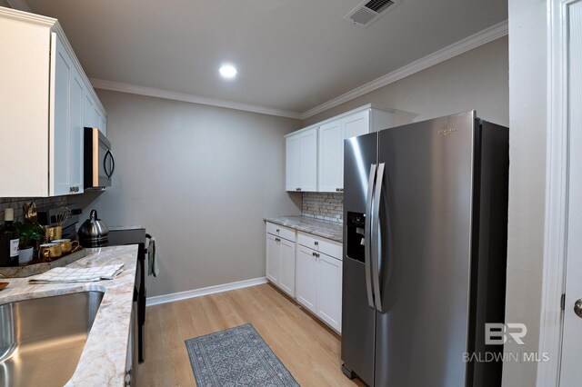 kitchen with visible vents, light wood-style flooring, white cabinetry, stainless steel fridge, and crown molding