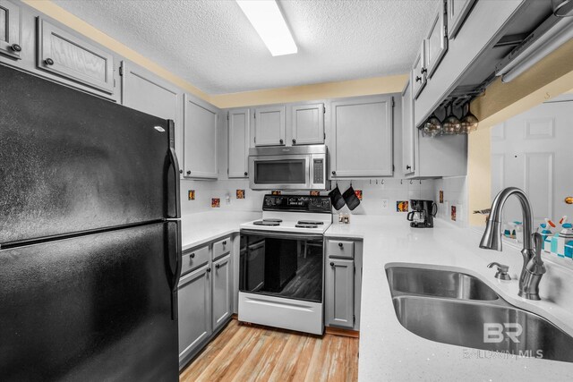 kitchen featuring black fridge, sink, backsplash, electric stove, and light hardwood / wood-style floors