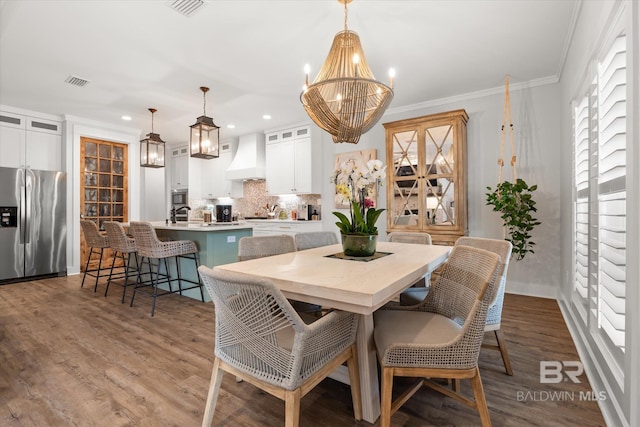 dining space with sink, an inviting chandelier, ornamental molding, and hardwood / wood-style floors