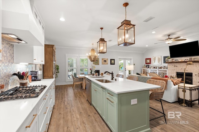 kitchen featuring stainless steel appliances, white cabinets, a fireplace, pendant lighting, and a kitchen island with sink