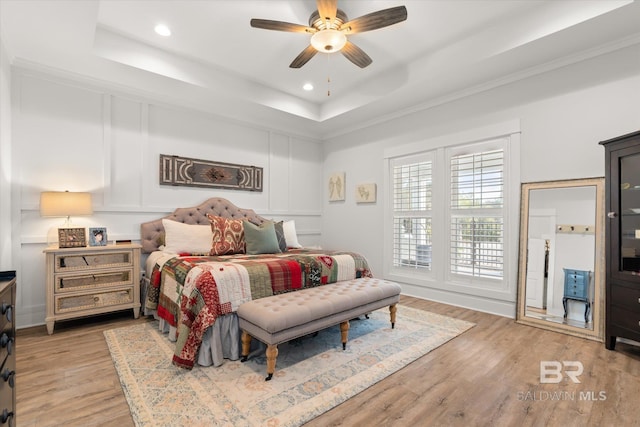 bedroom with ceiling fan, a tray ceiling, and light hardwood / wood-style flooring