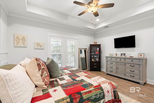 bedroom featuring ceiling fan, crown molding, light hardwood / wood-style flooring, and a raised ceiling