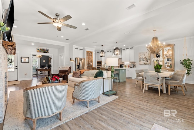 living room with ceiling fan with notable chandelier, ornamental molding, and light hardwood / wood-style flooring