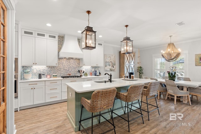 kitchen featuring premium range hood, gas cooktop, a kitchen island with sink, and white cabinetry