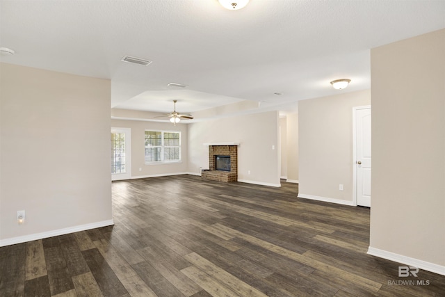 unfurnished living room with visible vents, a brick fireplace, baseboards, ceiling fan, and dark wood-style flooring