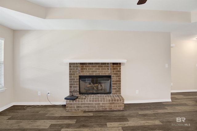 unfurnished living room featuring a brick fireplace, baseboards, and wood finished floors