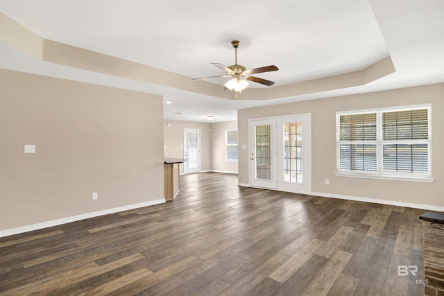 unfurnished living room with a tray ceiling, baseboards, and dark wood-style flooring