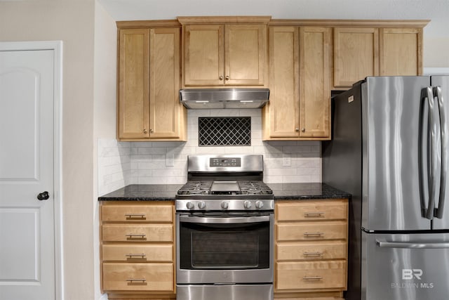 kitchen with under cabinet range hood, stainless steel appliances, dark stone counters, and tasteful backsplash