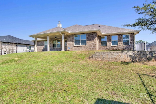 rear view of property featuring a ceiling fan, fence, a chimney, a lawn, and brick siding