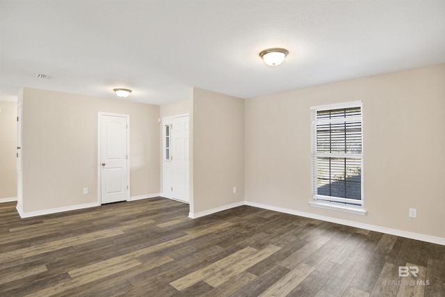 spare room with visible vents, baseboards, and dark wood-style flooring