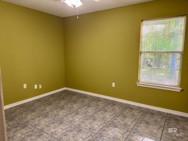 empty room featuring dark tile patterned flooring, a wealth of natural light, a ceiling fan, and a textured ceiling