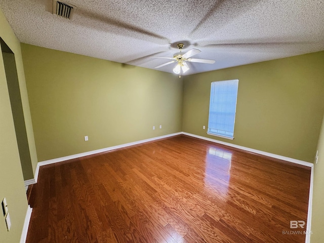 spare room with ceiling fan, a textured ceiling, visible vents, wood finished floors, and baseboards