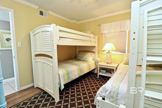 bedroom featuring baseboards, wood finished floors, visible vents, and crown molding