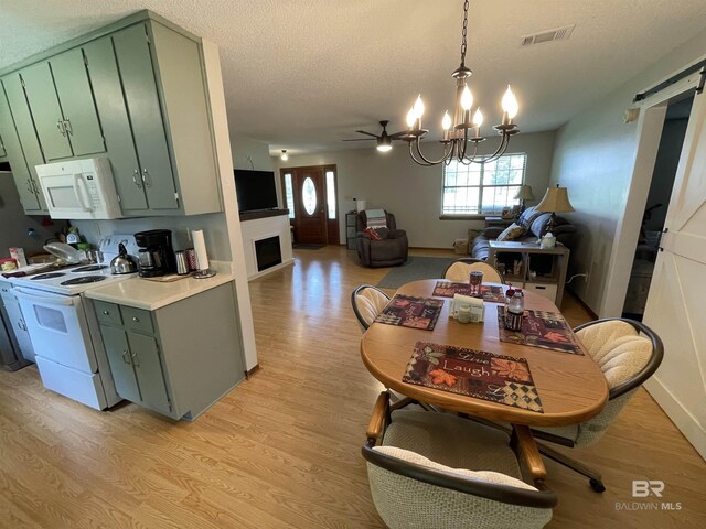 dining room with ceiling fan with notable chandelier, a textured ceiling, and light hardwood / wood-style floors