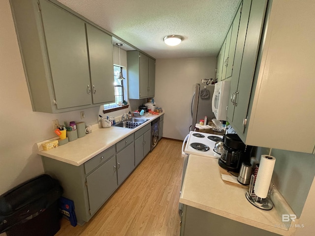 kitchen with a textured ceiling, stainless steel appliances, light hardwood / wood-style floors, green cabinetry, and sink