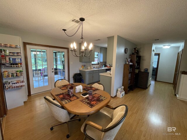 dining space featuring an inviting chandelier, light hardwood / wood-style floors, a textured ceiling, and a wealth of natural light