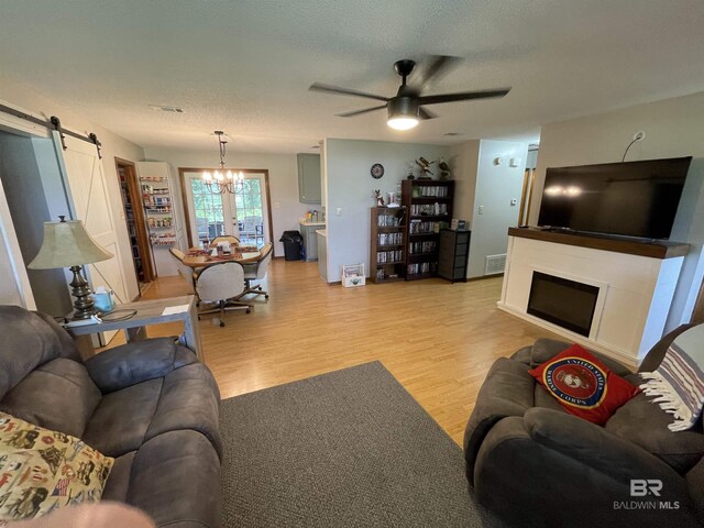 living room featuring ceiling fan with notable chandelier, a textured ceiling, a barn door, and light hardwood / wood-style flooring