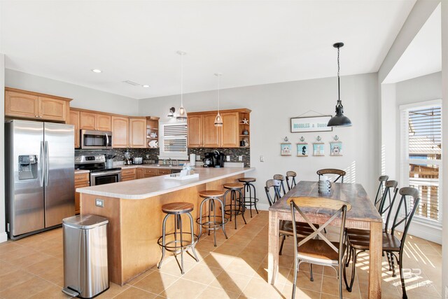 kitchen with plenty of natural light, tasteful backsplash, decorative light fixtures, and appliances with stainless steel finishes