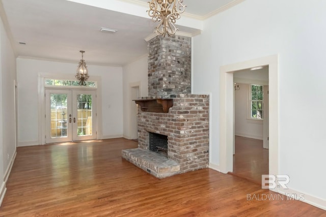 unfurnished living room featuring wood-type flooring, ornamental molding, a brick fireplace, and french doors