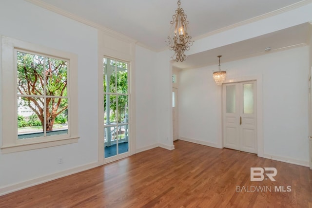 empty room featuring crown molding, an inviting chandelier, and wood-type flooring