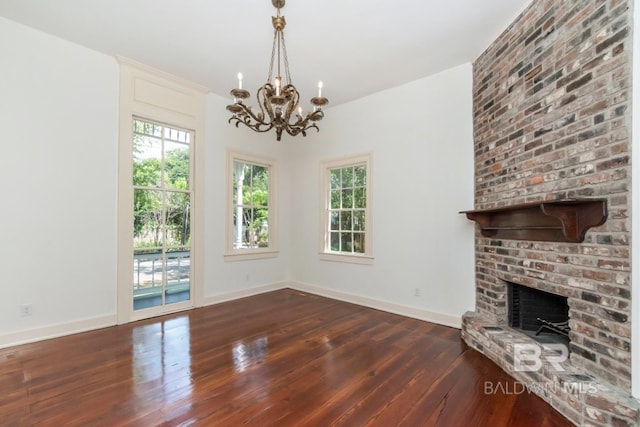 unfurnished living room featuring dark hardwood / wood-style flooring, a chandelier, and a brick fireplace