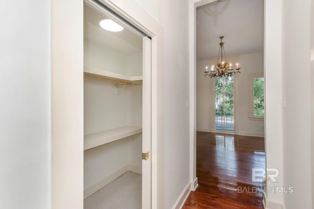 hallway featuring dark wood-style flooring, baseboards, and a notable chandelier