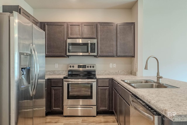 kitchen featuring kitchen peninsula, stainless steel appliances, light wood-type flooring, dark brown cabinetry, and sink