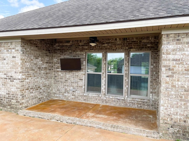 doorway to property with ceiling fan, a shingled roof, and brick siding