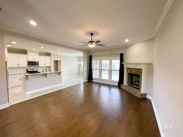 unfurnished living room with ornamental molding, light wood finished floors, a ceiling fan, and baseboards