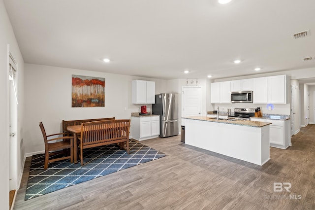 kitchen featuring appliances with stainless steel finishes, light stone counters, a kitchen island with sink, wood-type flooring, and white cabinets