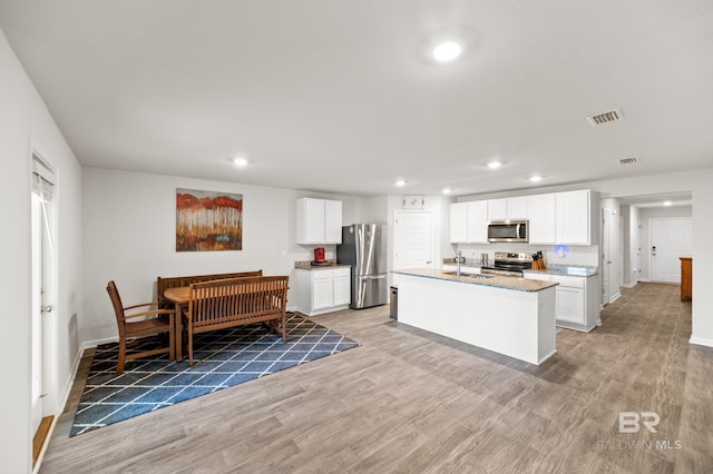 kitchen with stainless steel appliances, light stone counters, an island with sink, light hardwood / wood-style floors, and white cabinets