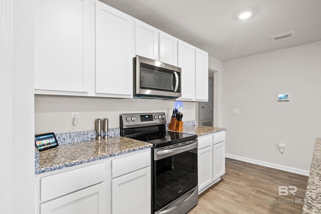 kitchen with light stone countertops, white cabinets, stainless steel appliances, and light hardwood / wood-style floors